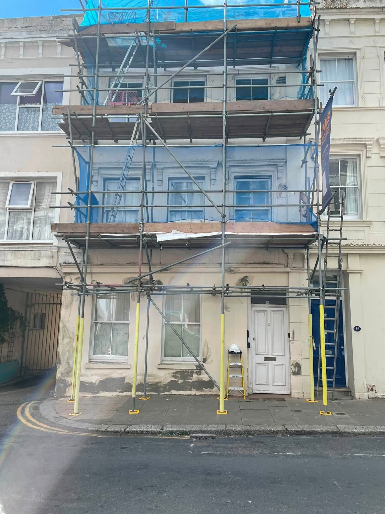 Scaffolded townhouse with patched, flaking render before decorating