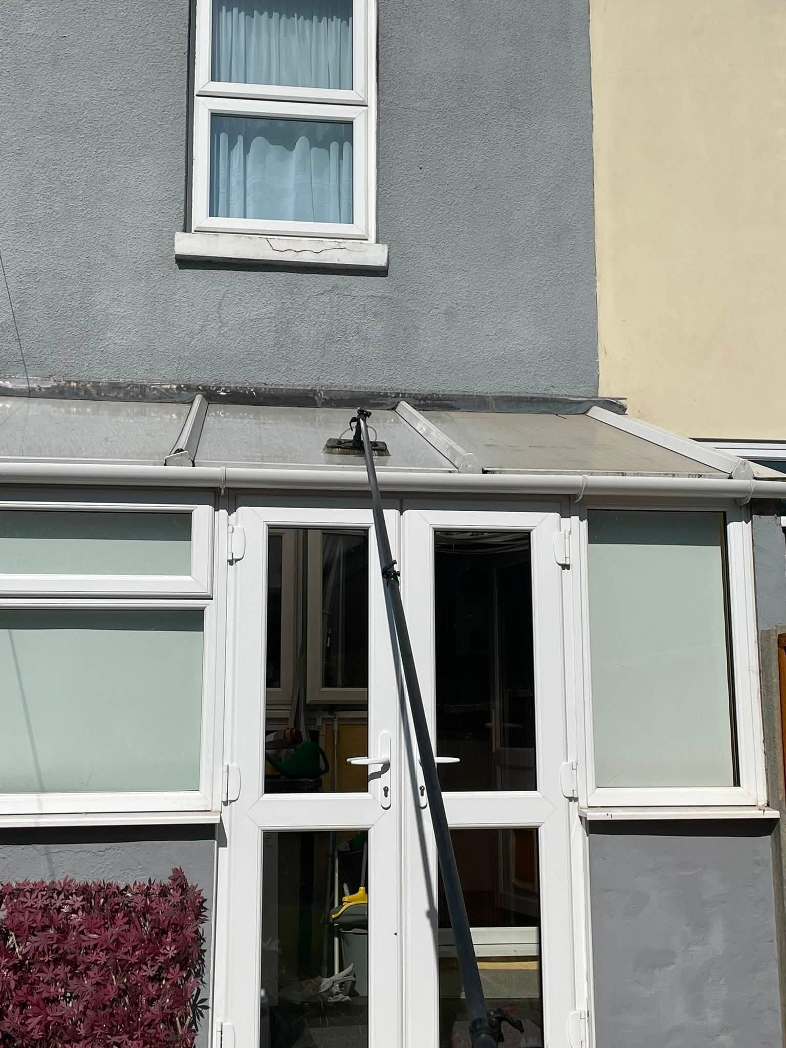 Water-fed pole washing a rendered wall and conservatory